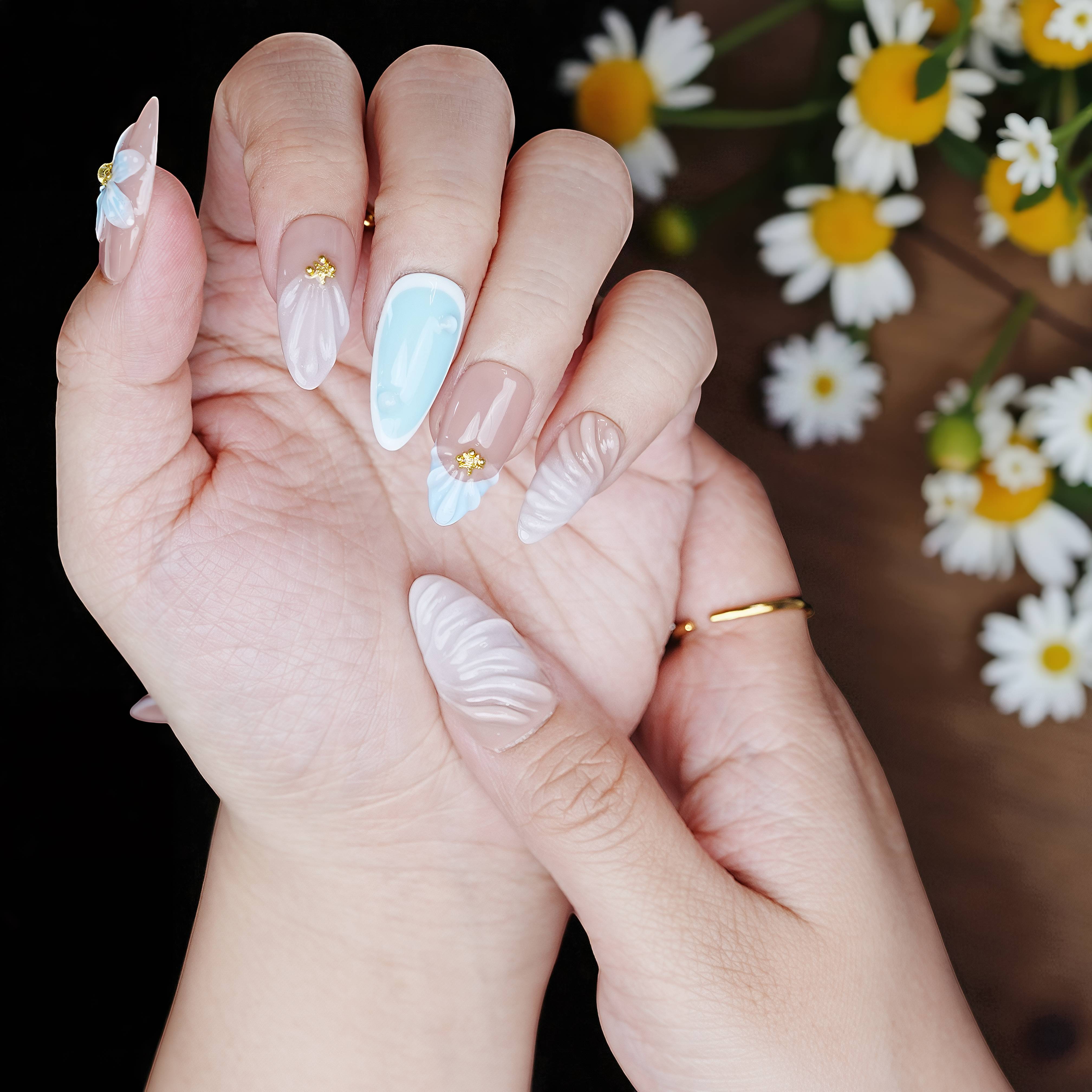 Sculpted nails held over floral daisies, showing spring vibe and soft-glow gloss.