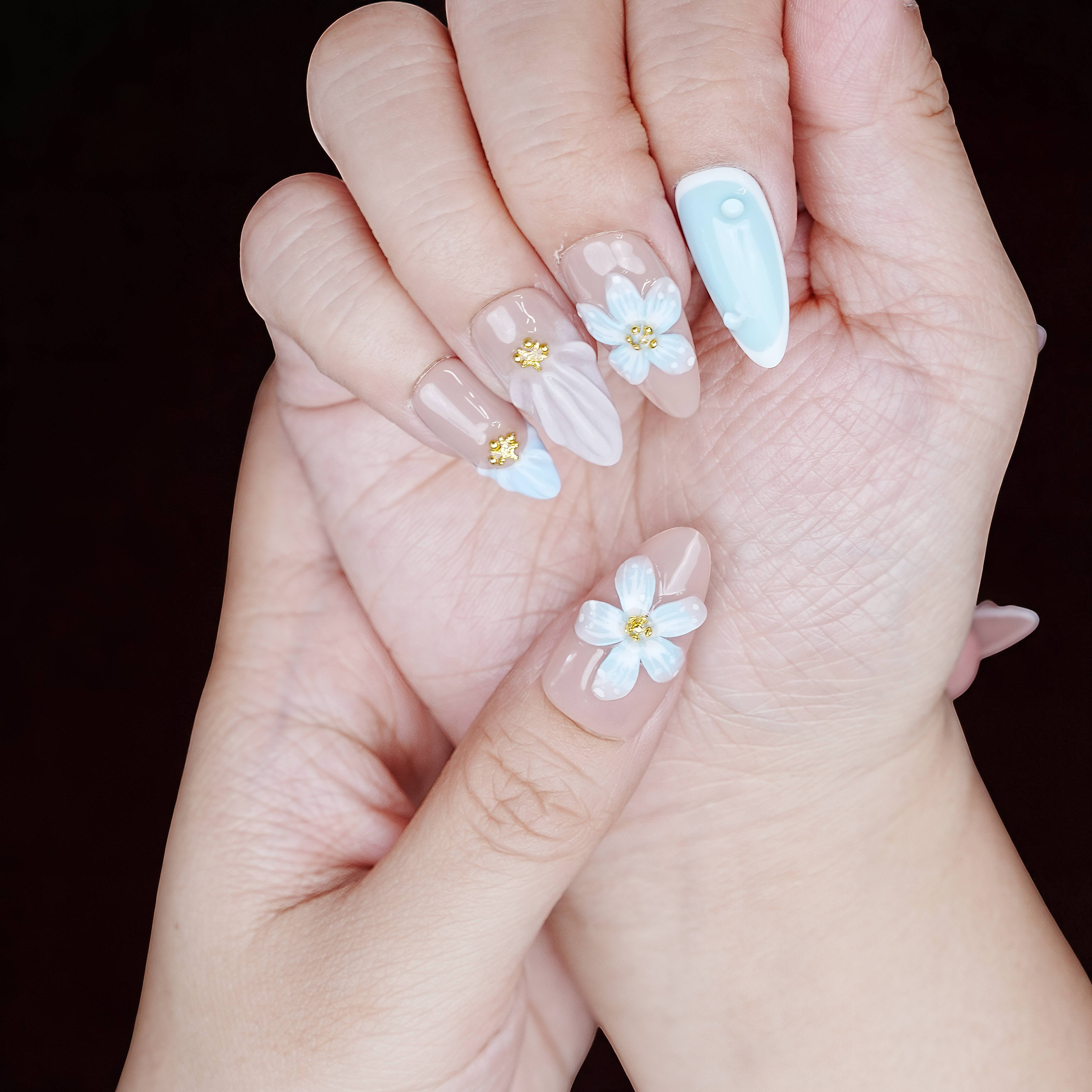 Soft-touch hand pose showing full set with sculpted shell finish, baby blue tip, and soft flower center.