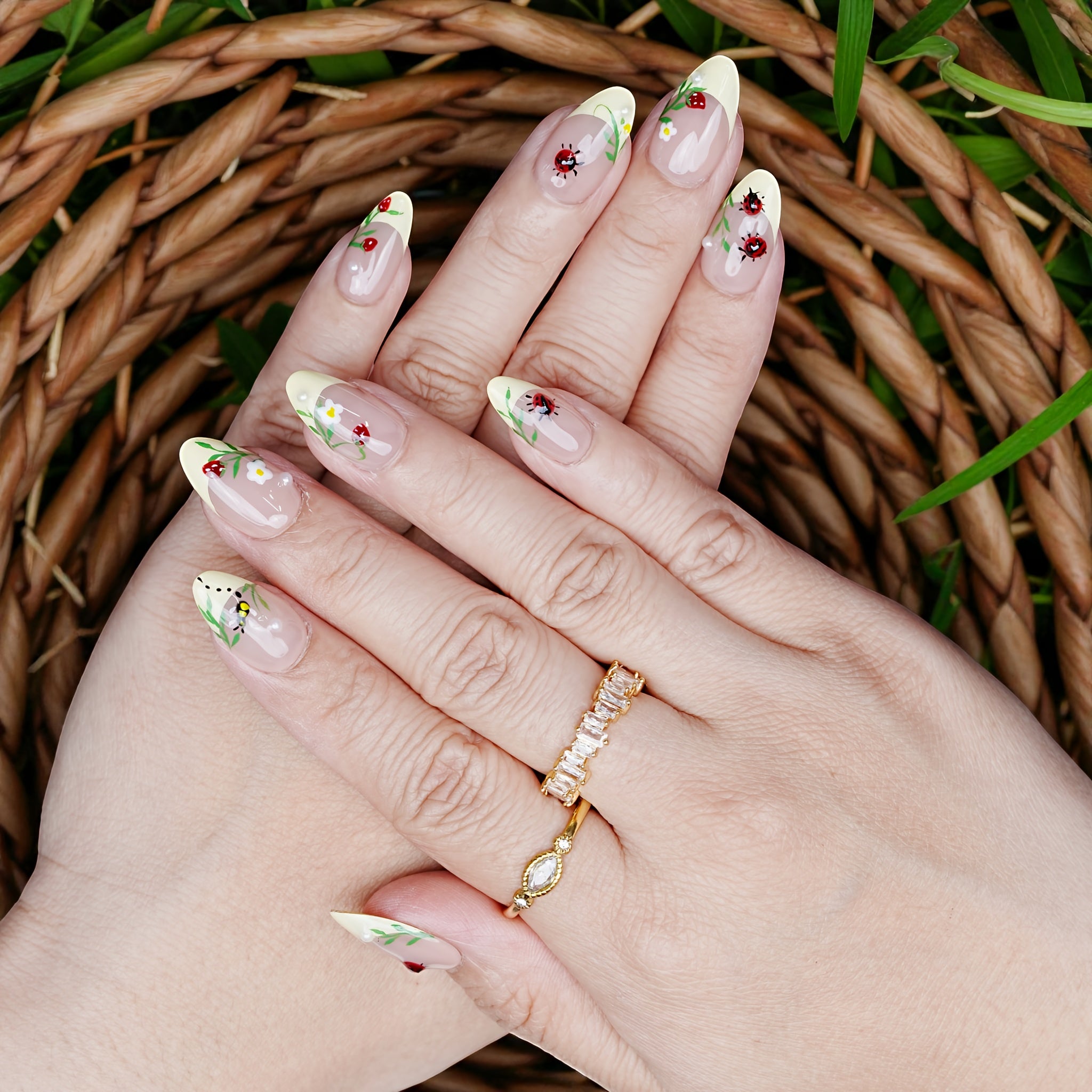 Full hand display of Garden Picnic nails with yellow French tips, floral designs, and crawling ladybug accents.