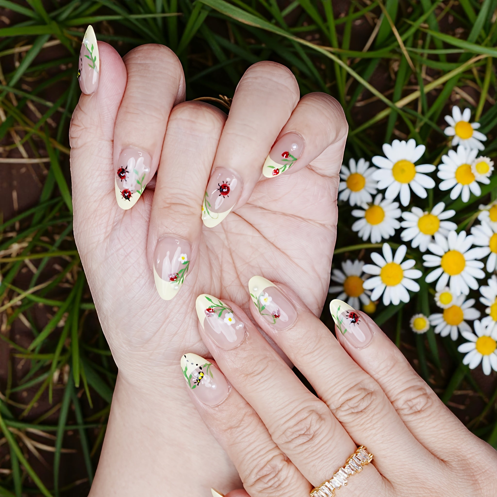 Spring flat lay of nails worn in garden setting, showcasing bee and flower details across both hands.