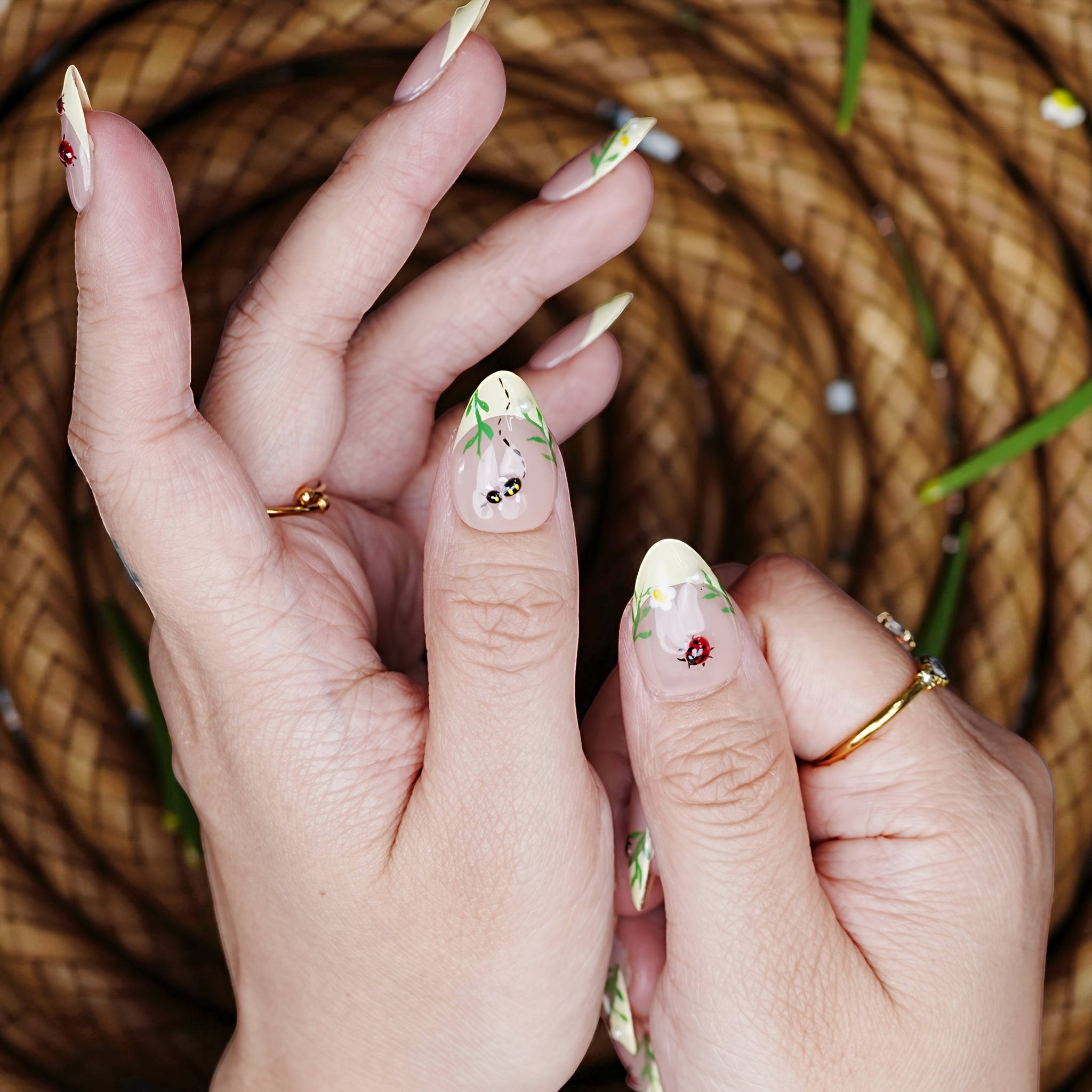 Thumb-focused hand pose with bumblebee art and grass linework over sheer nude polish.