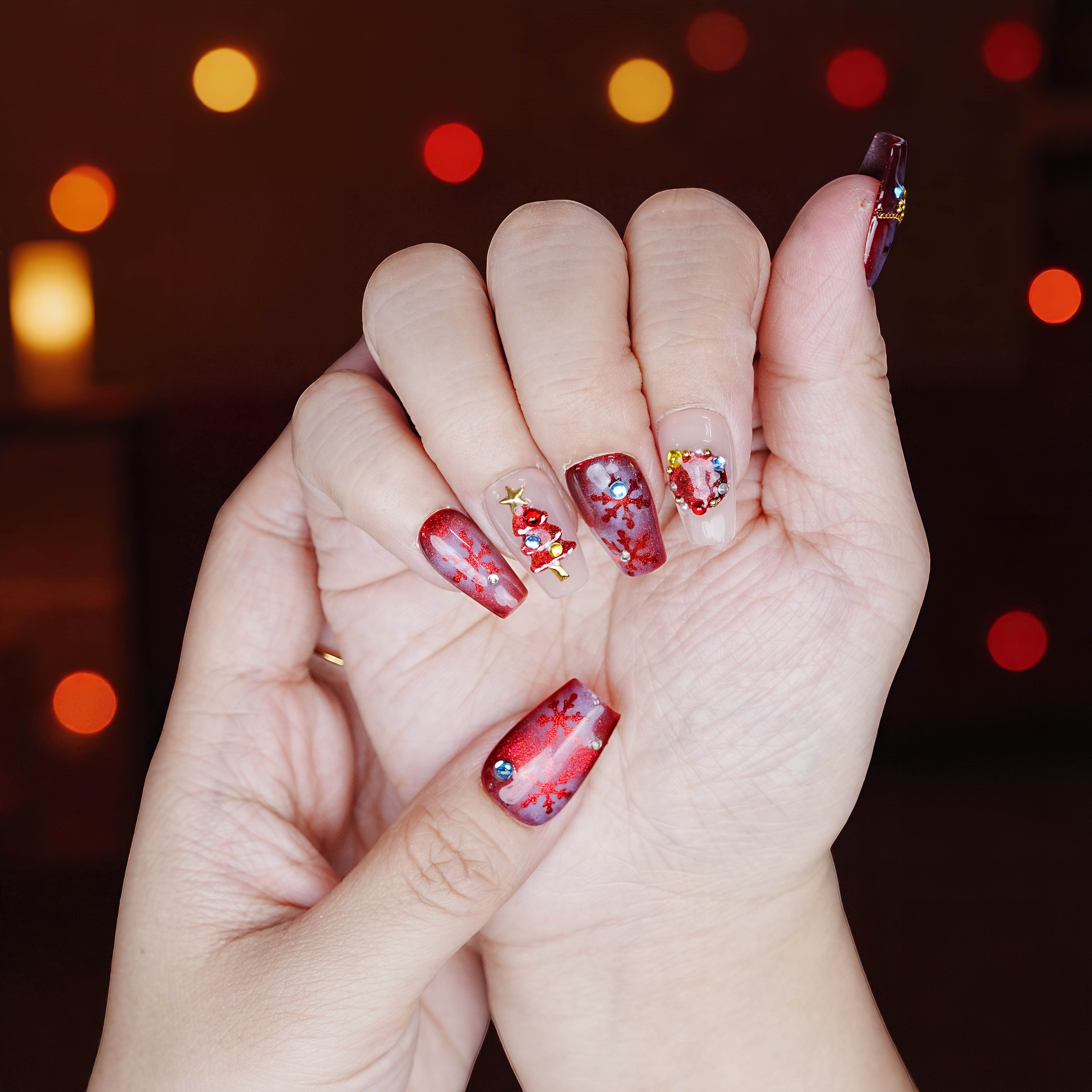 Hand displaying red press on nails with snowflake glitter and Christmas decoration accents under warm lights
