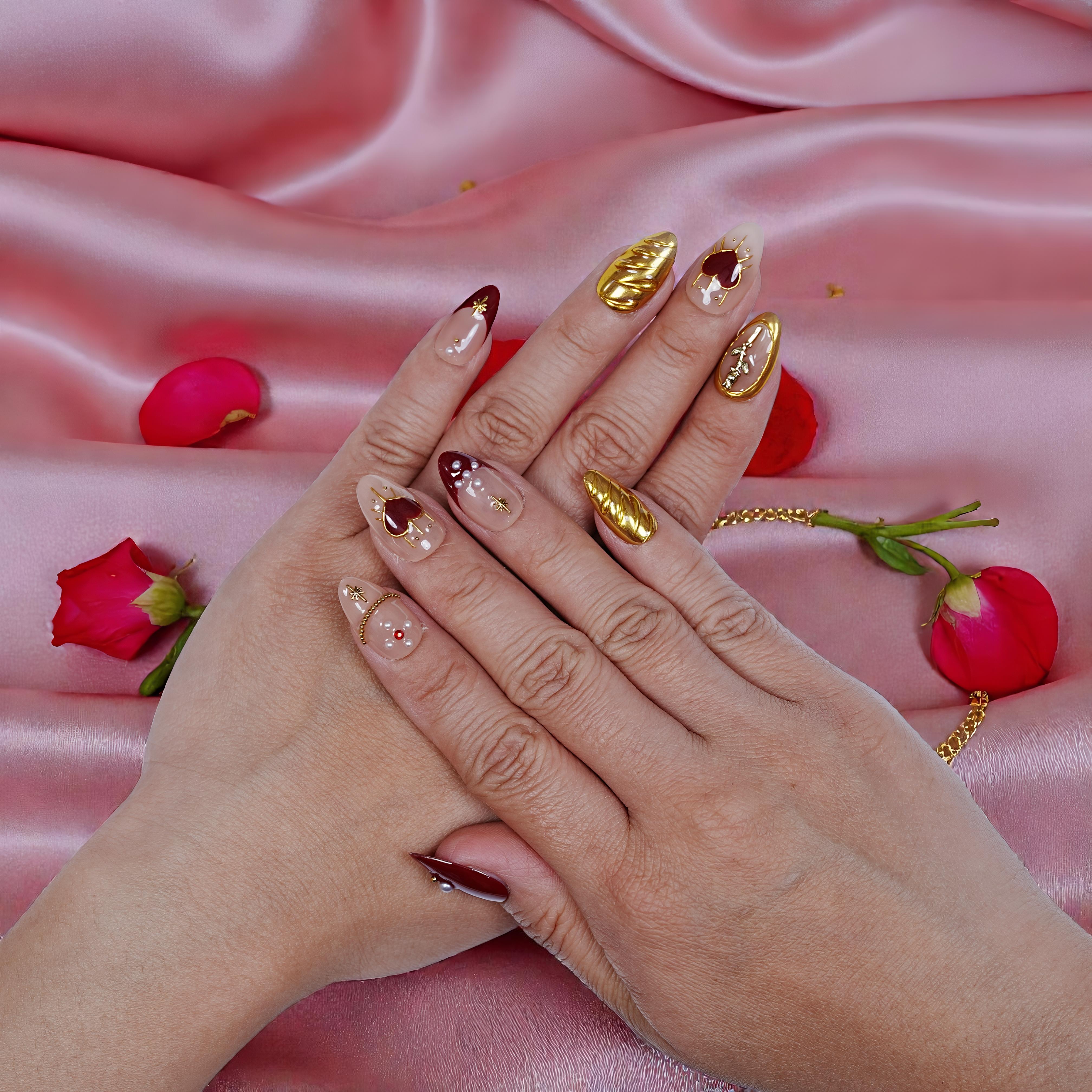 Handmade press on nails with gold and burgundy designs on hands, pink satin background, rose petals