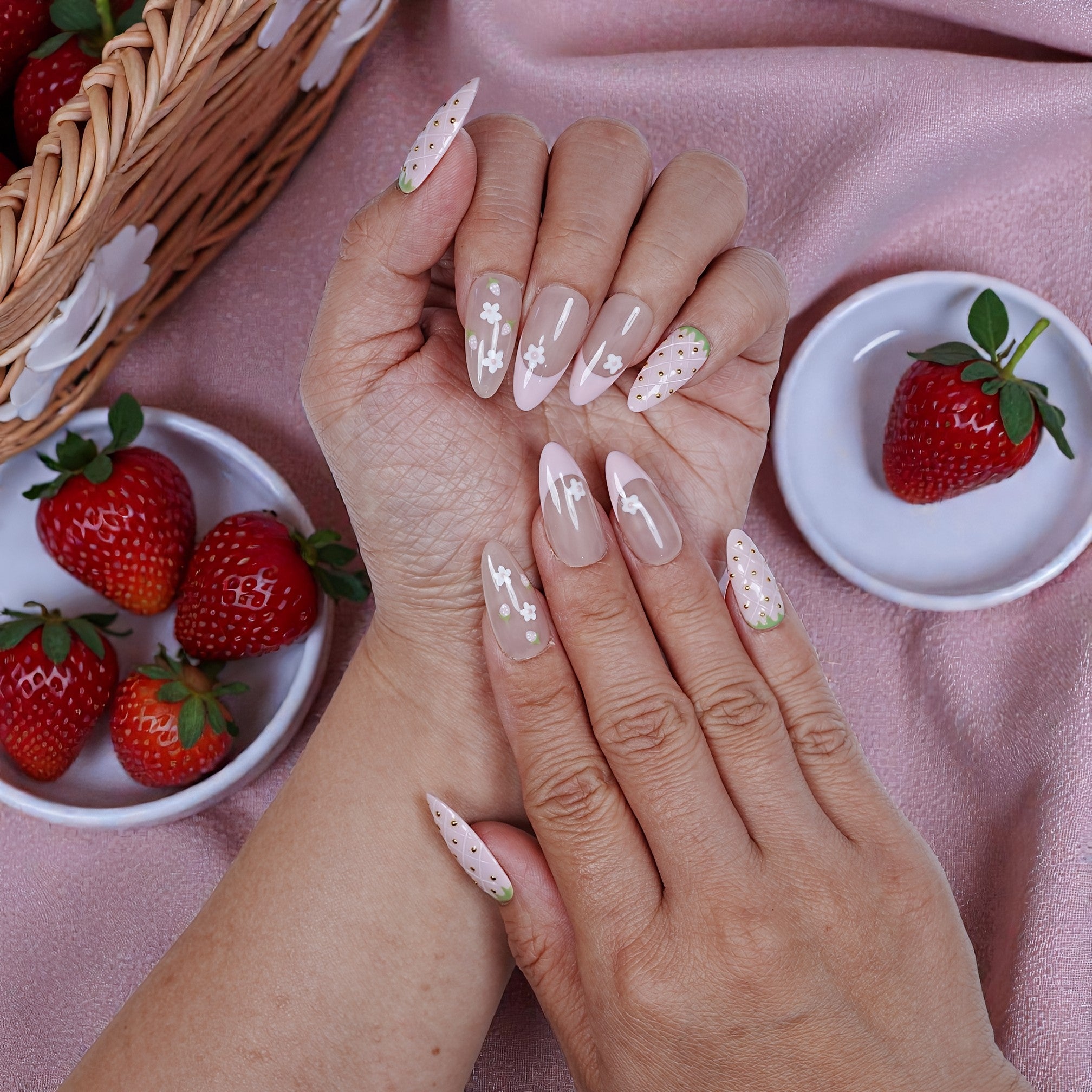 Hand with long pink floral and strawberry press on nails, strawberries and basket nearby