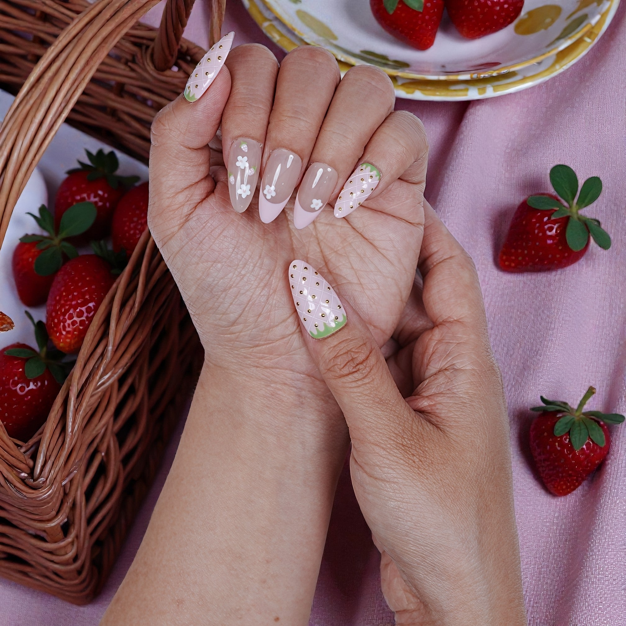 Hand with strawberry-themed handmade press on nails, basket of strawberries in background