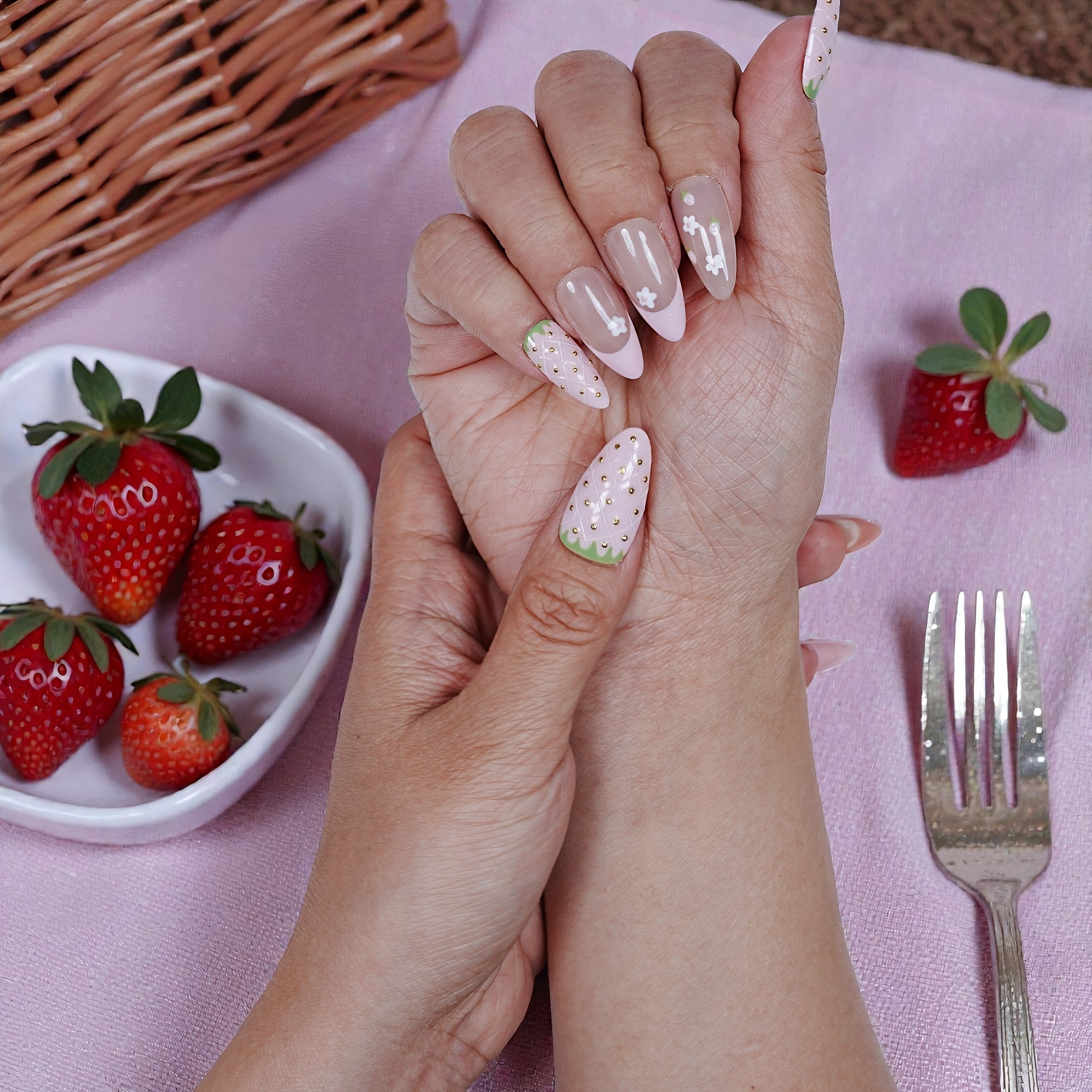 Hand with premium handmade press on nails featuring strawberry designs, beside fresh strawberries.