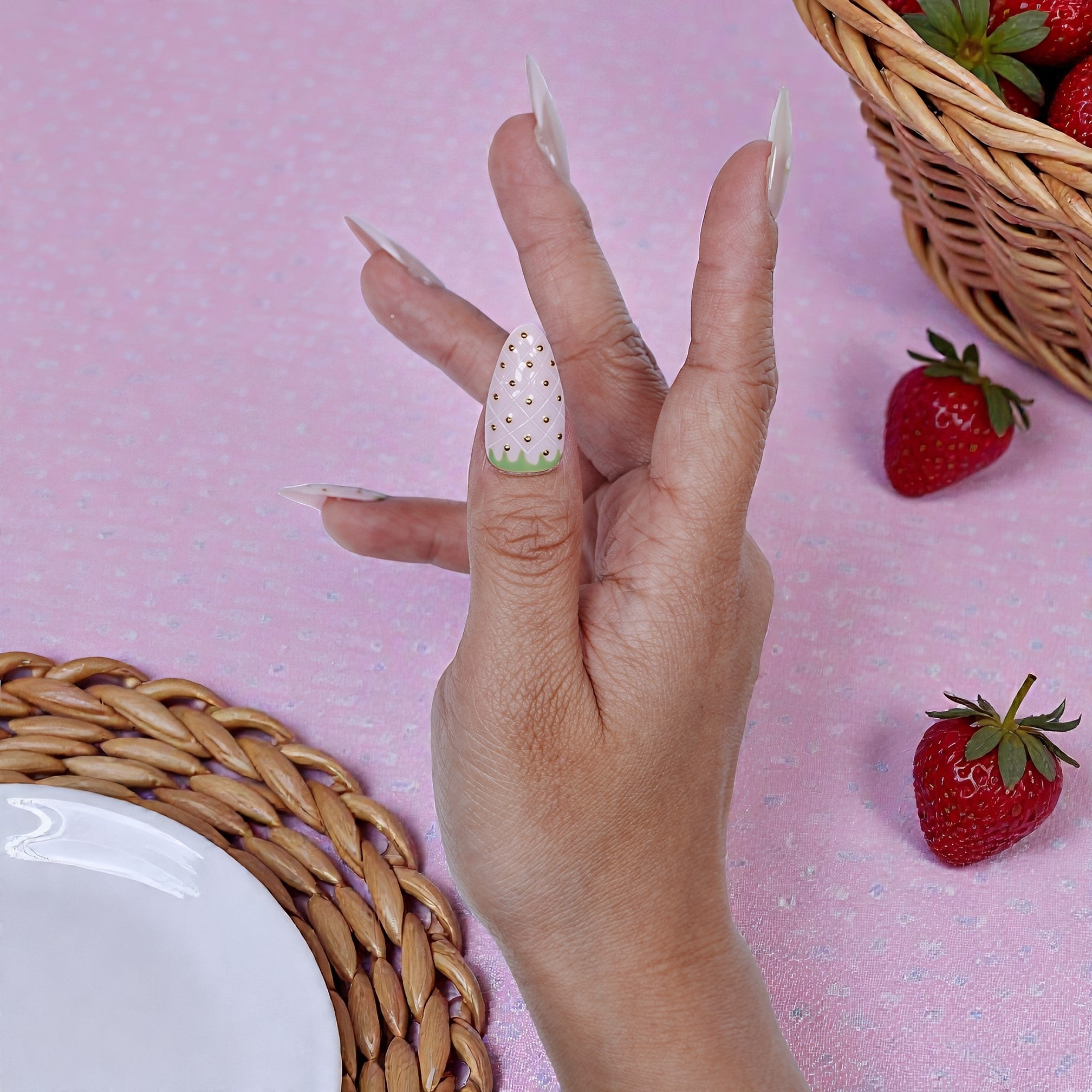 Hand with premium handmade press on nails, strawberry design, on pink table with strawberries