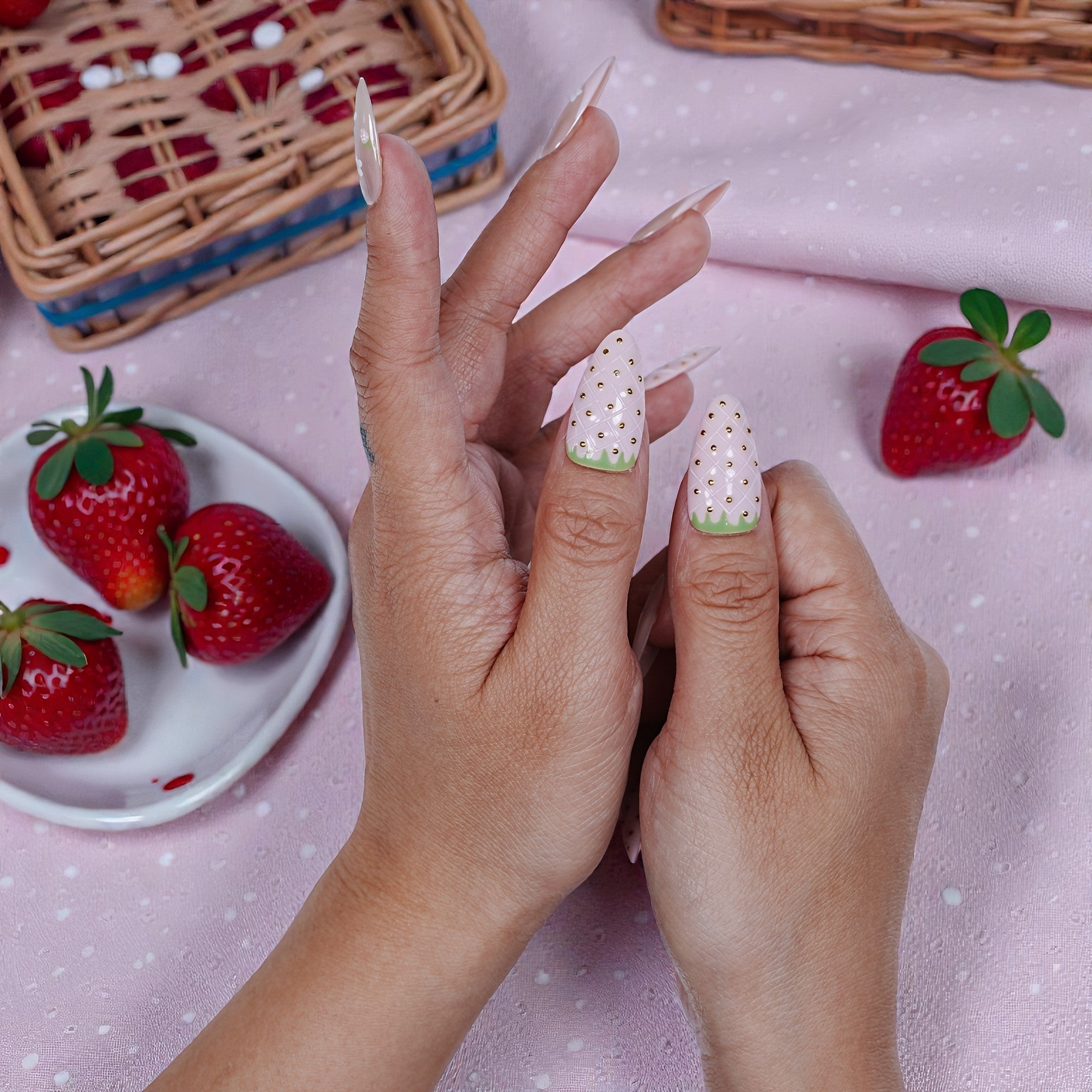 Hand with premium handmade press on nails featuring strawberry-inspired nail art, pink background, strawberries nearby.