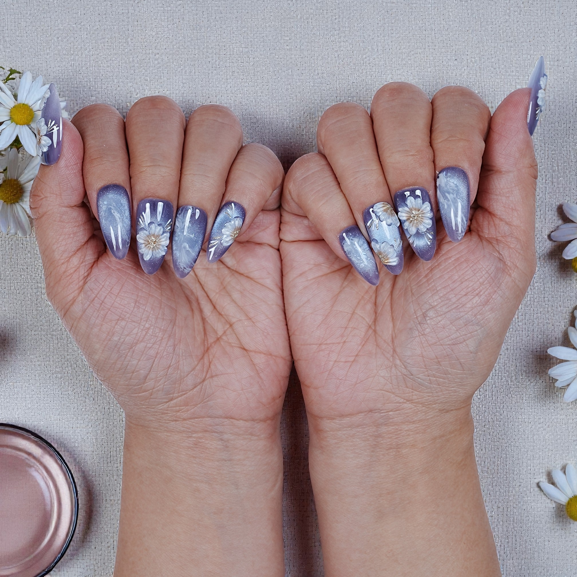 Hand displaying purple press on nails with white daisy floral designs, Dress For Nails