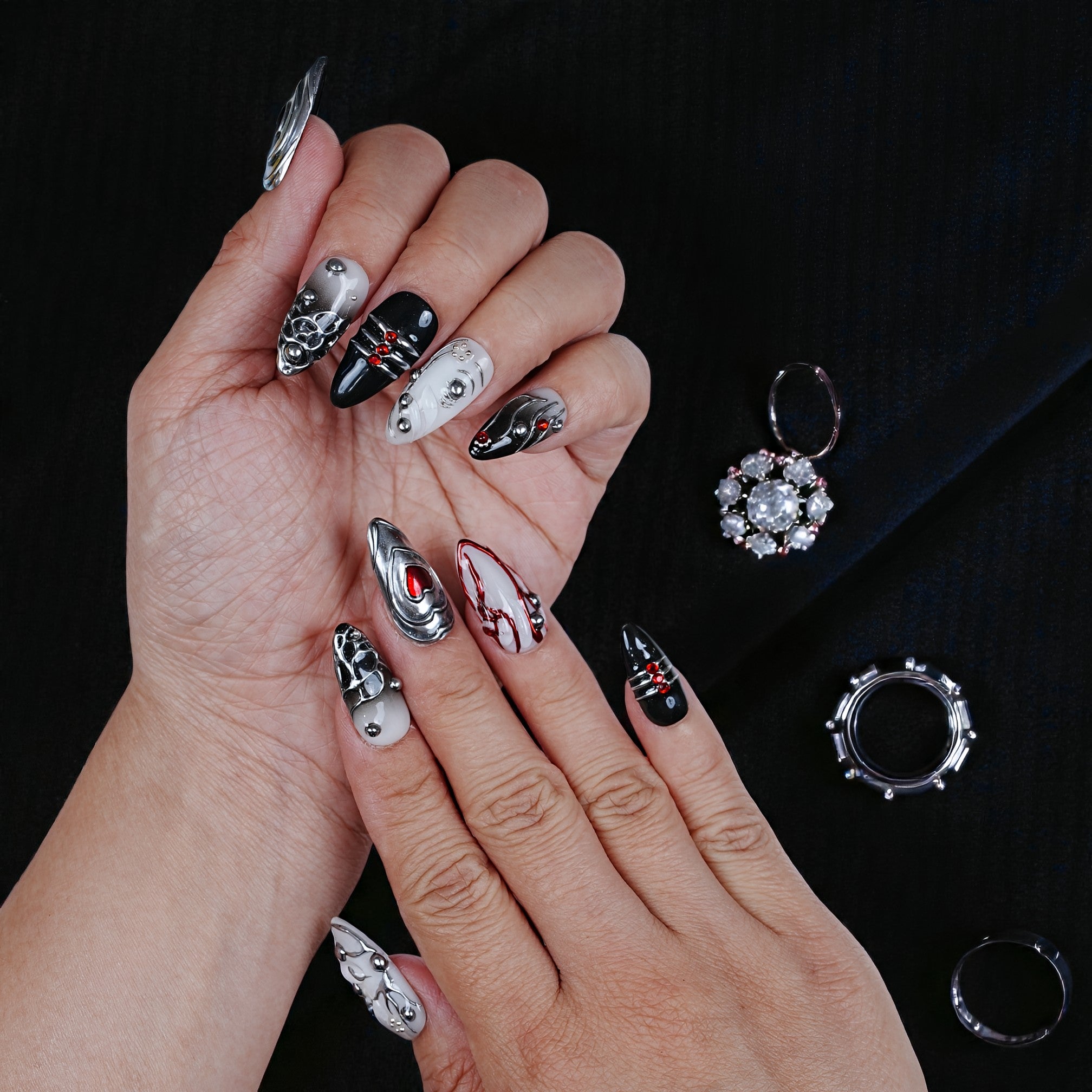 Hand with black, white, and silver 3D press on nails with jewel accents on black background