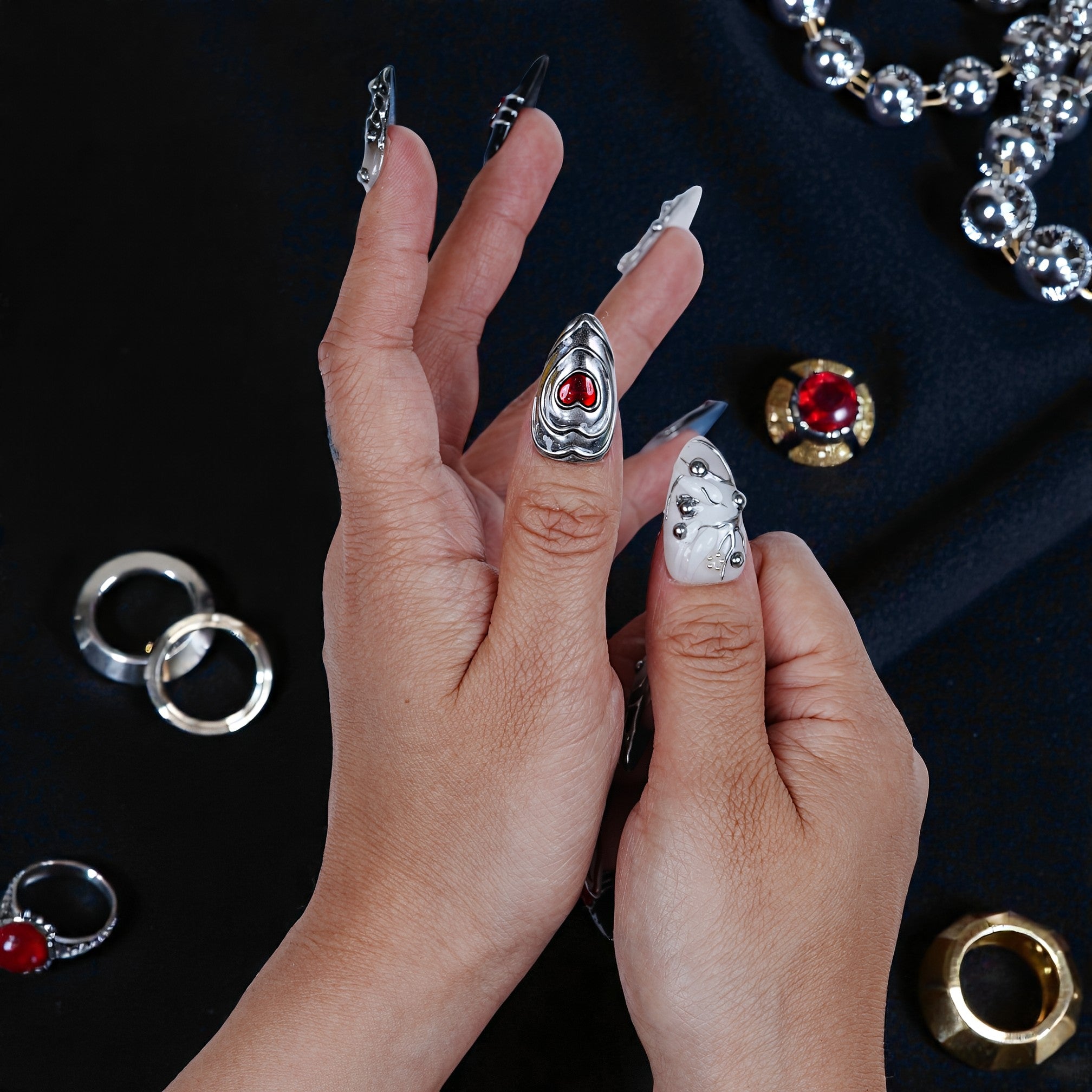 Hand with metallic silver and white press on nails, gemstone detail, surrounded by rings and jewelry.