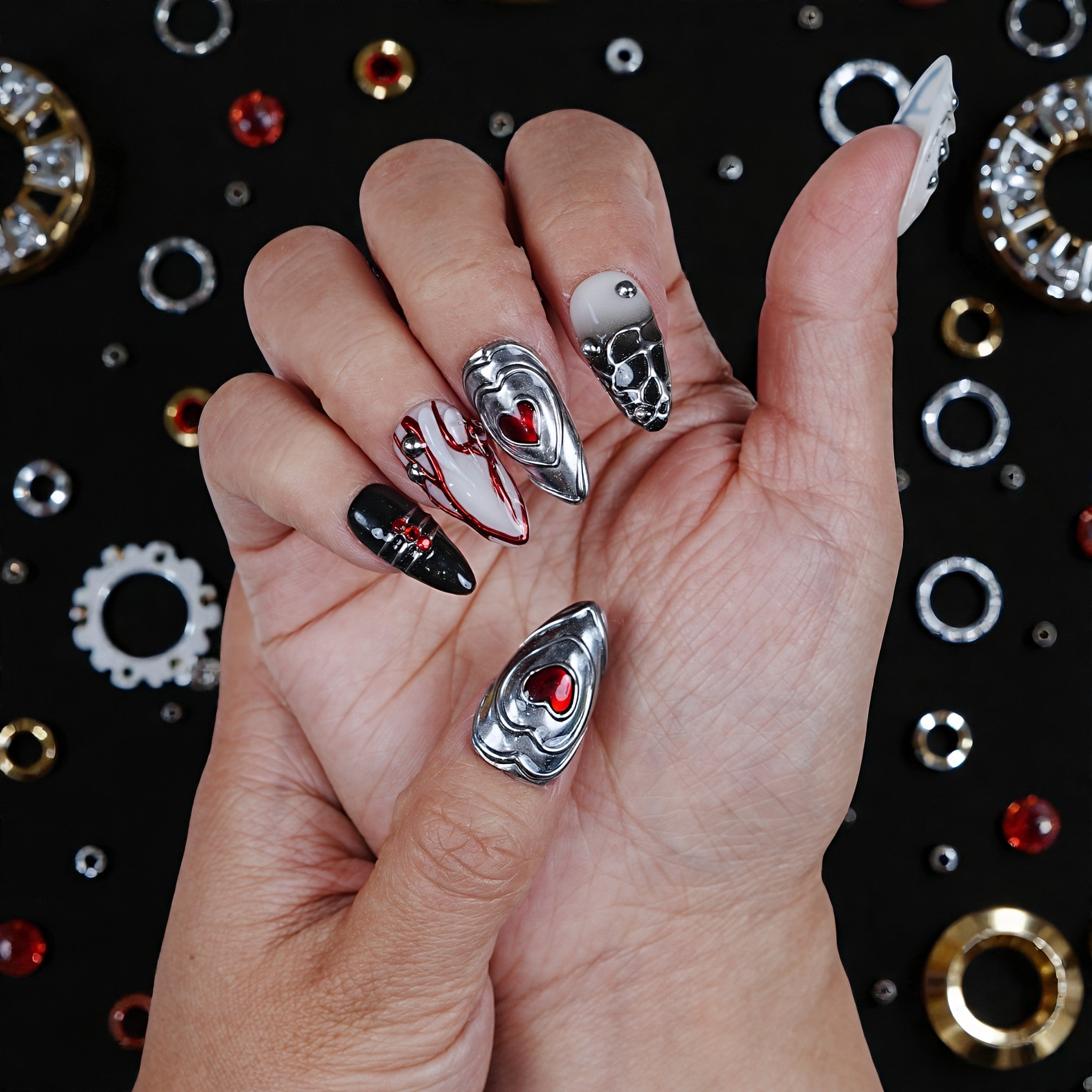 Hand with metallic heart-themed handmade press on nails, surrounded by nail art gems