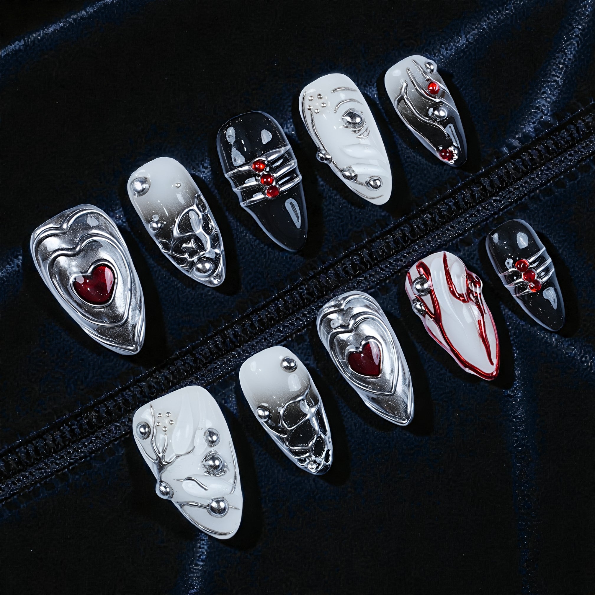 Handmade press on nails with chrome, heart, and red accent designs on black fabric