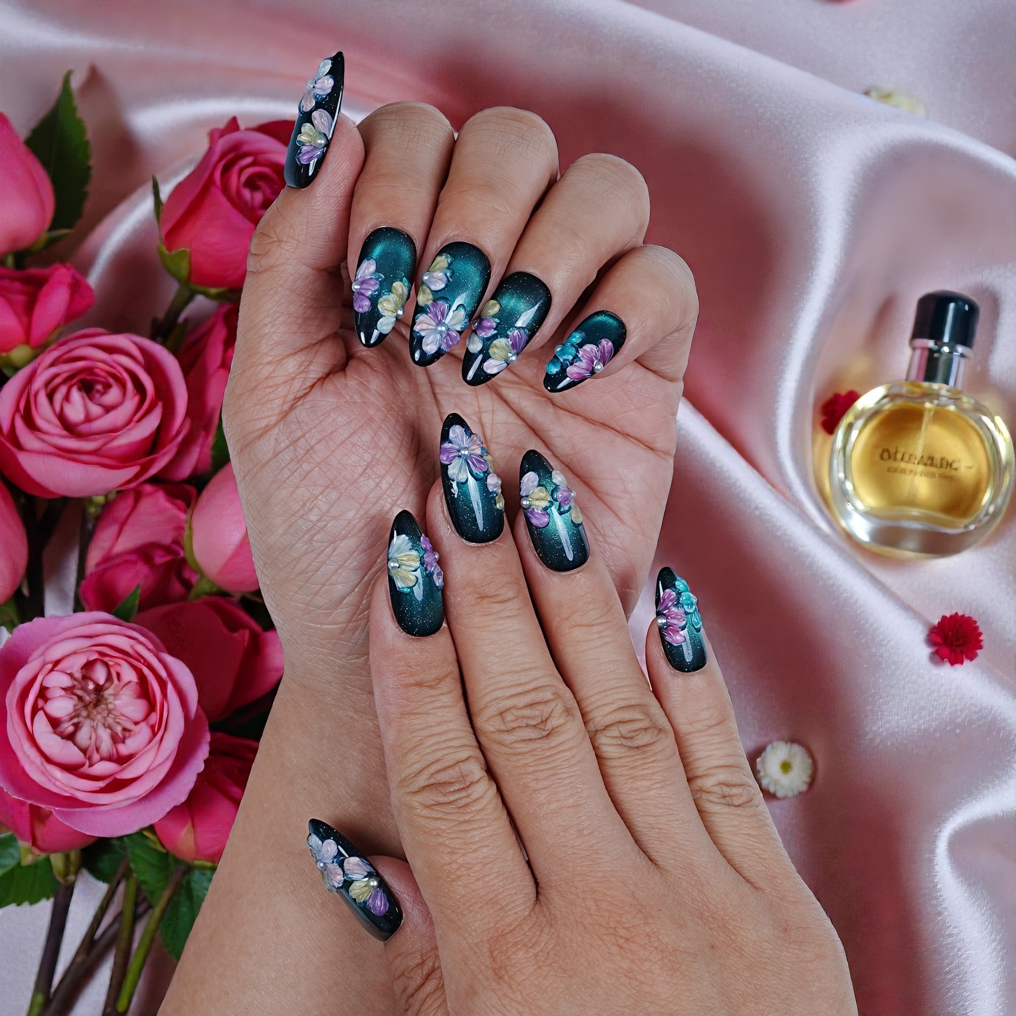 Hand with premium handmade floral press on nails, pink roses, and perfume on silk background