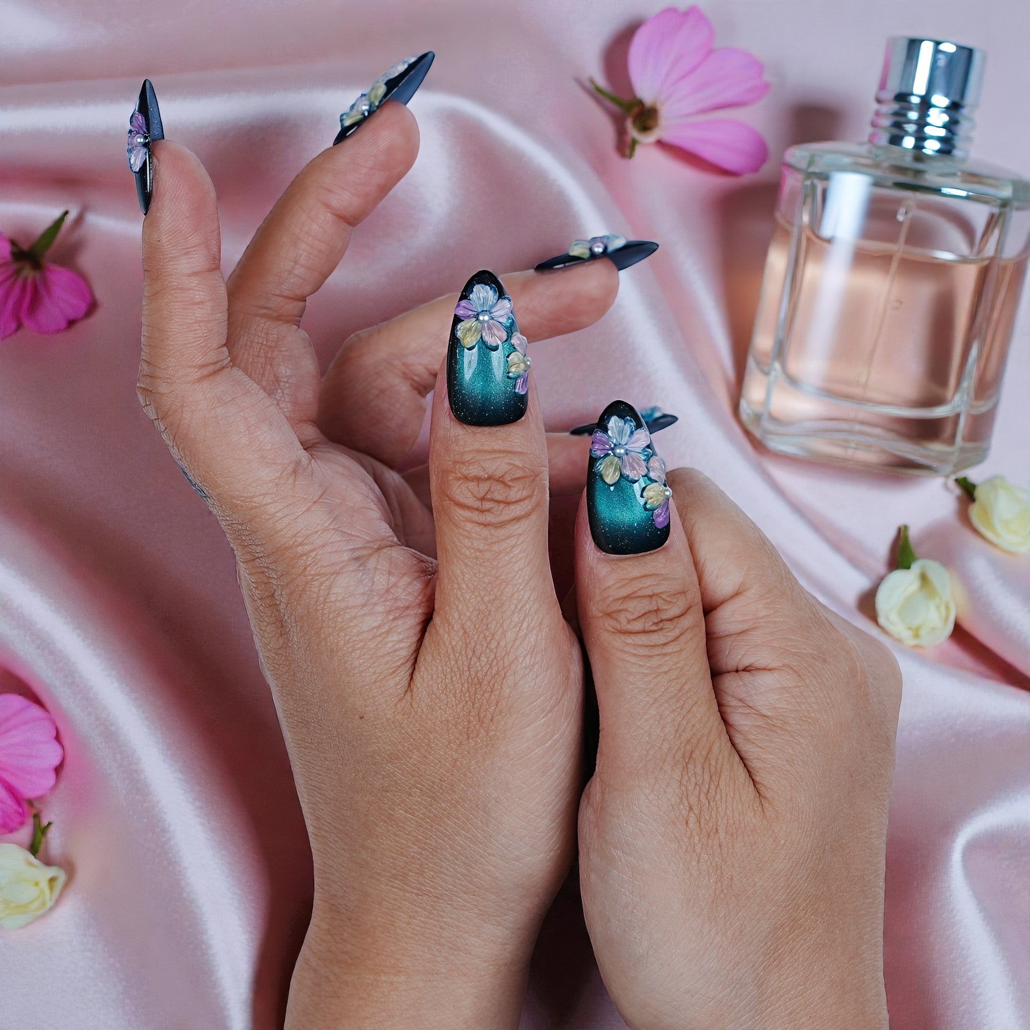 Hand with premium handmade press on nails featuring 3D floral design, on silk with flowers and perfume.