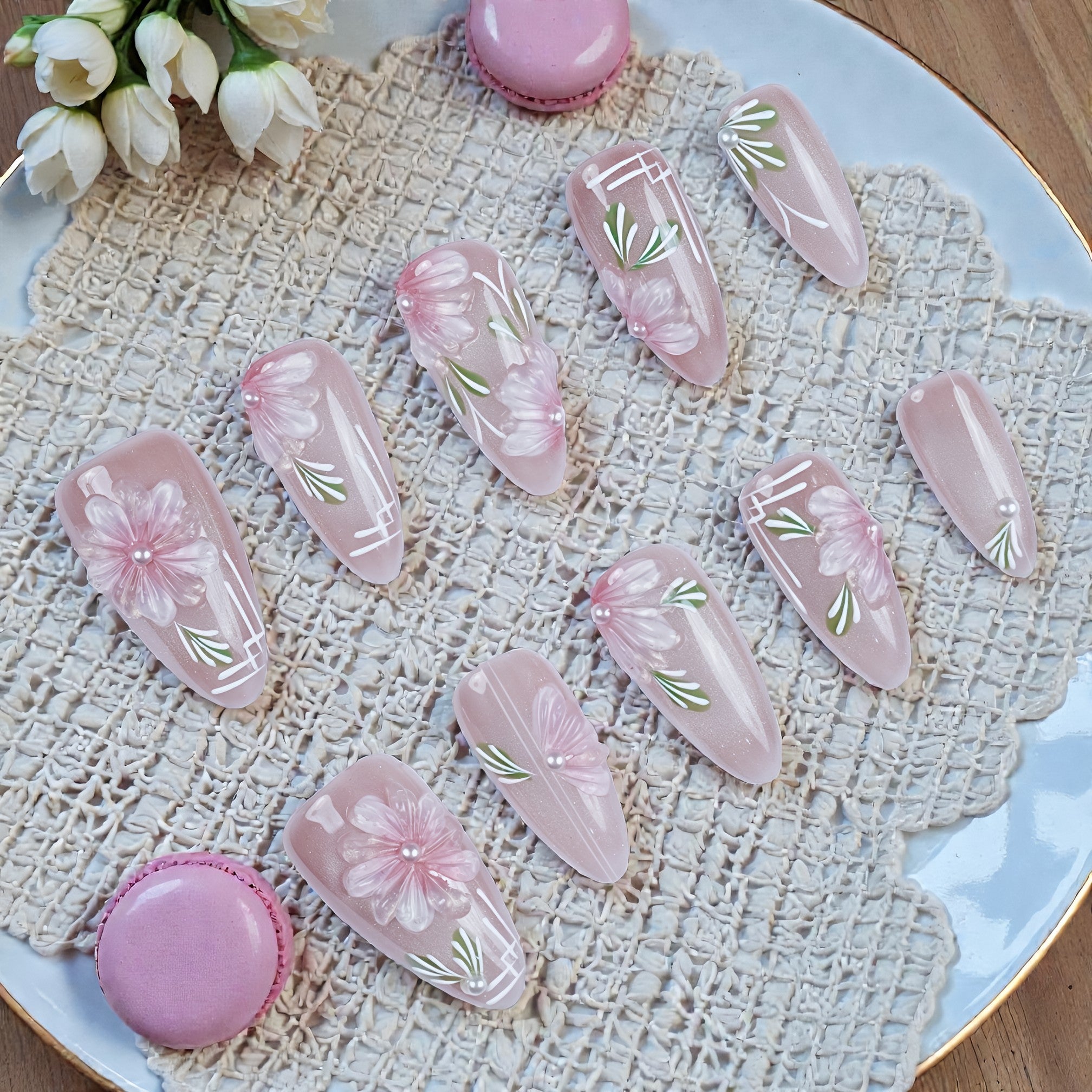 Pink floral handmade press on nails with white accents, arranged on a lace doily plate.