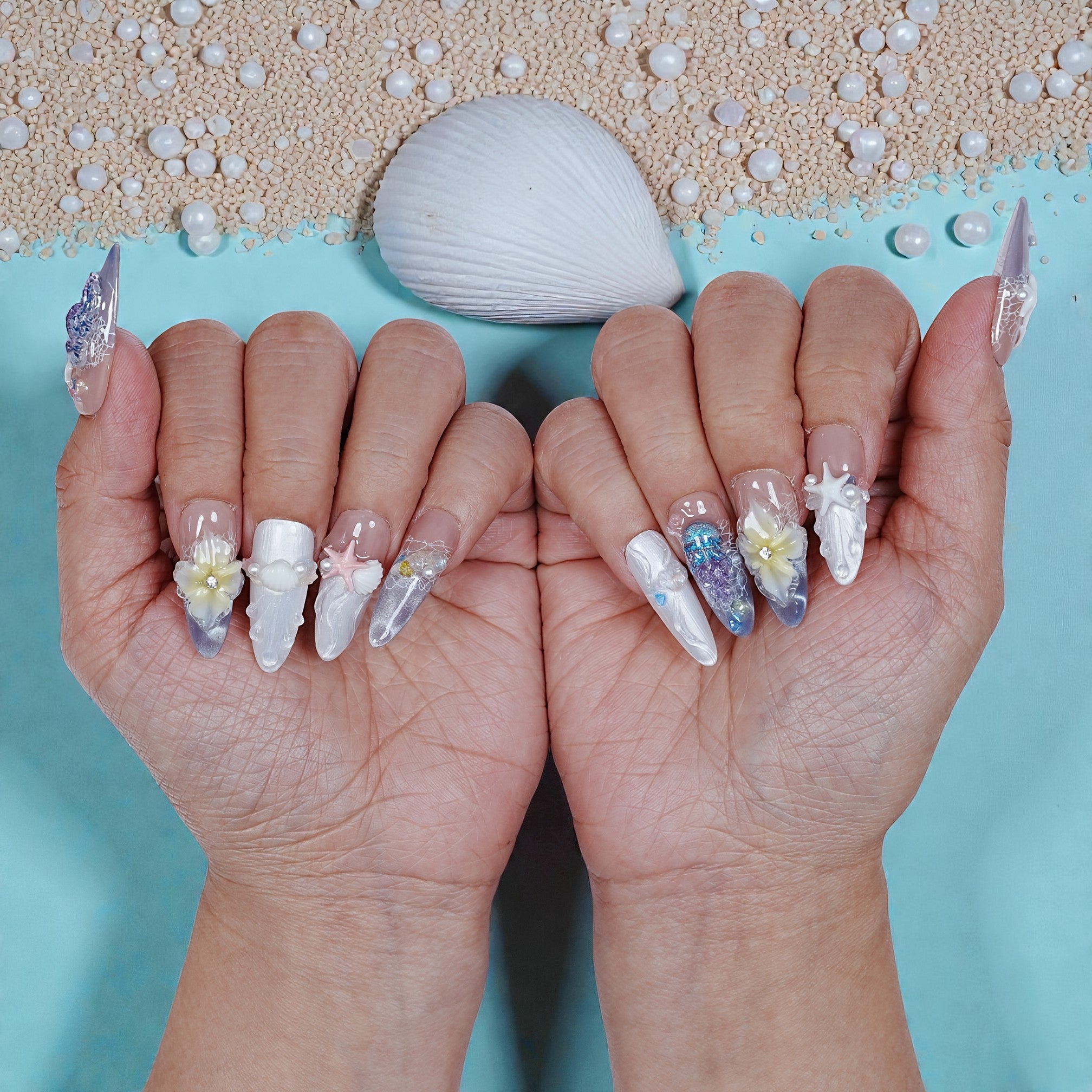 Hands with premium handmade press on nails, ocean-inspired 3D nail art, seashell and pearls