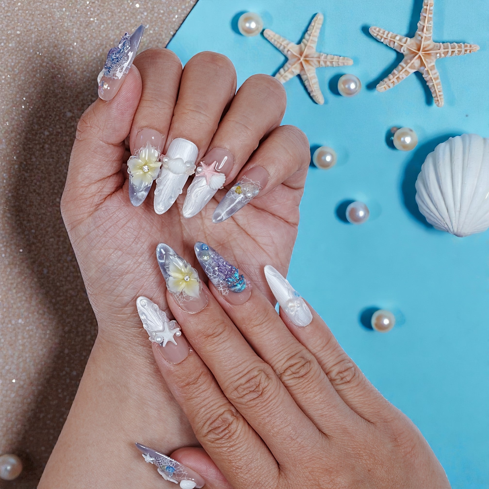 Hand with premium handmade beach-themed press on nails featuring shells and flowers