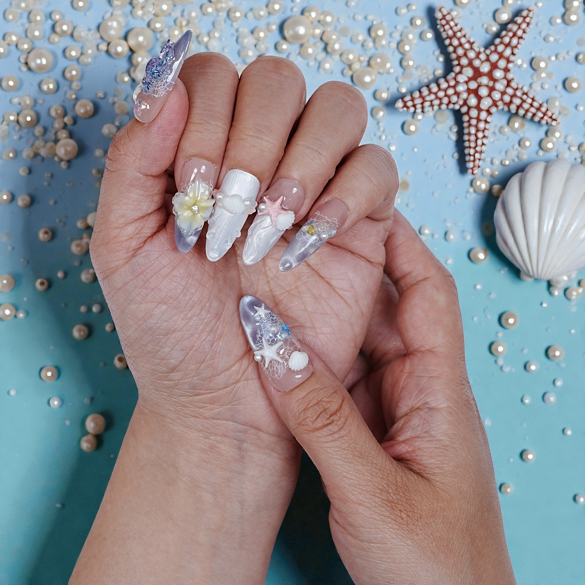 Hand holding premium handmade press on nails with ocean-themed 3D designs and pastel decorations