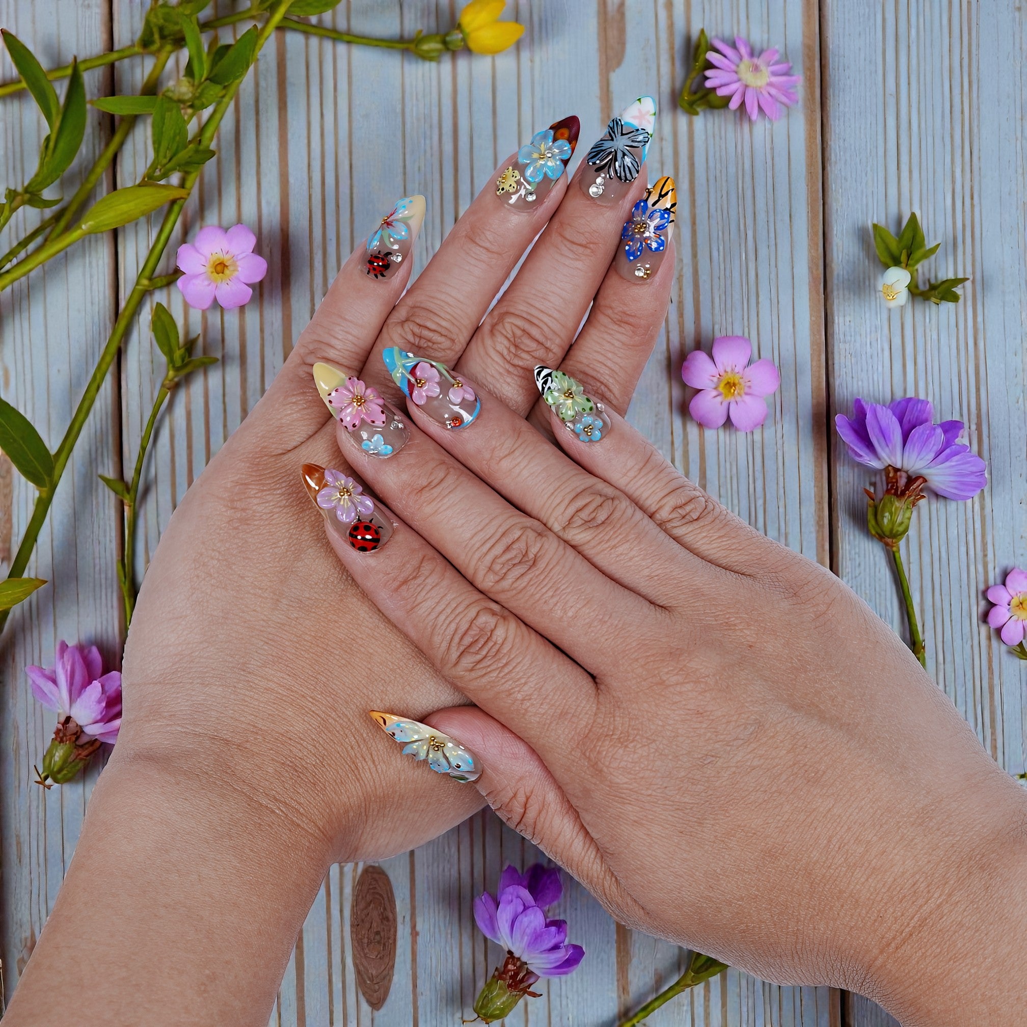 Hands with premium handmade floral press on nails, surrounded by flowers on wooden background