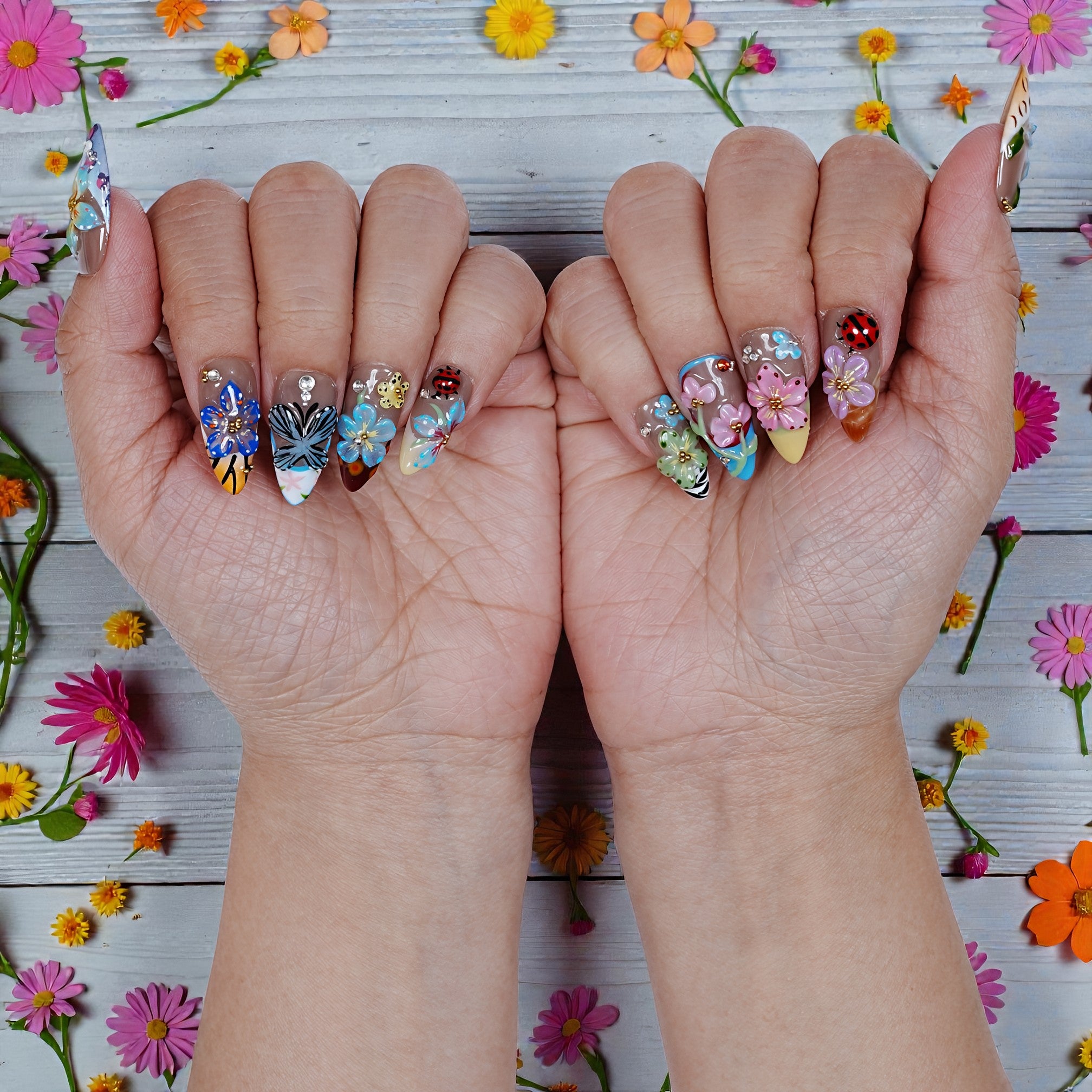 Hands with colorful handmade press on nails featuring 3D floral and butterfly designs