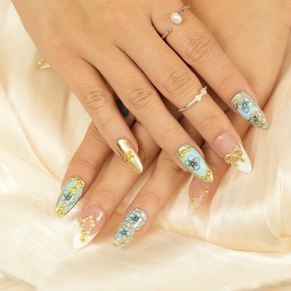 Close-up of blue and gold luxury press on nails with 3D bow and pearl accent, thumb pose