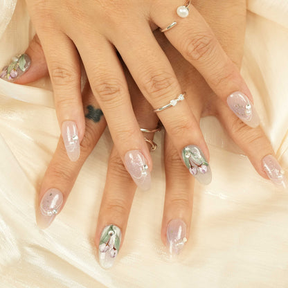 Thumb close-up with sage green nail, showcasing 3D purple flowers, pearl and rhinestone embellishments