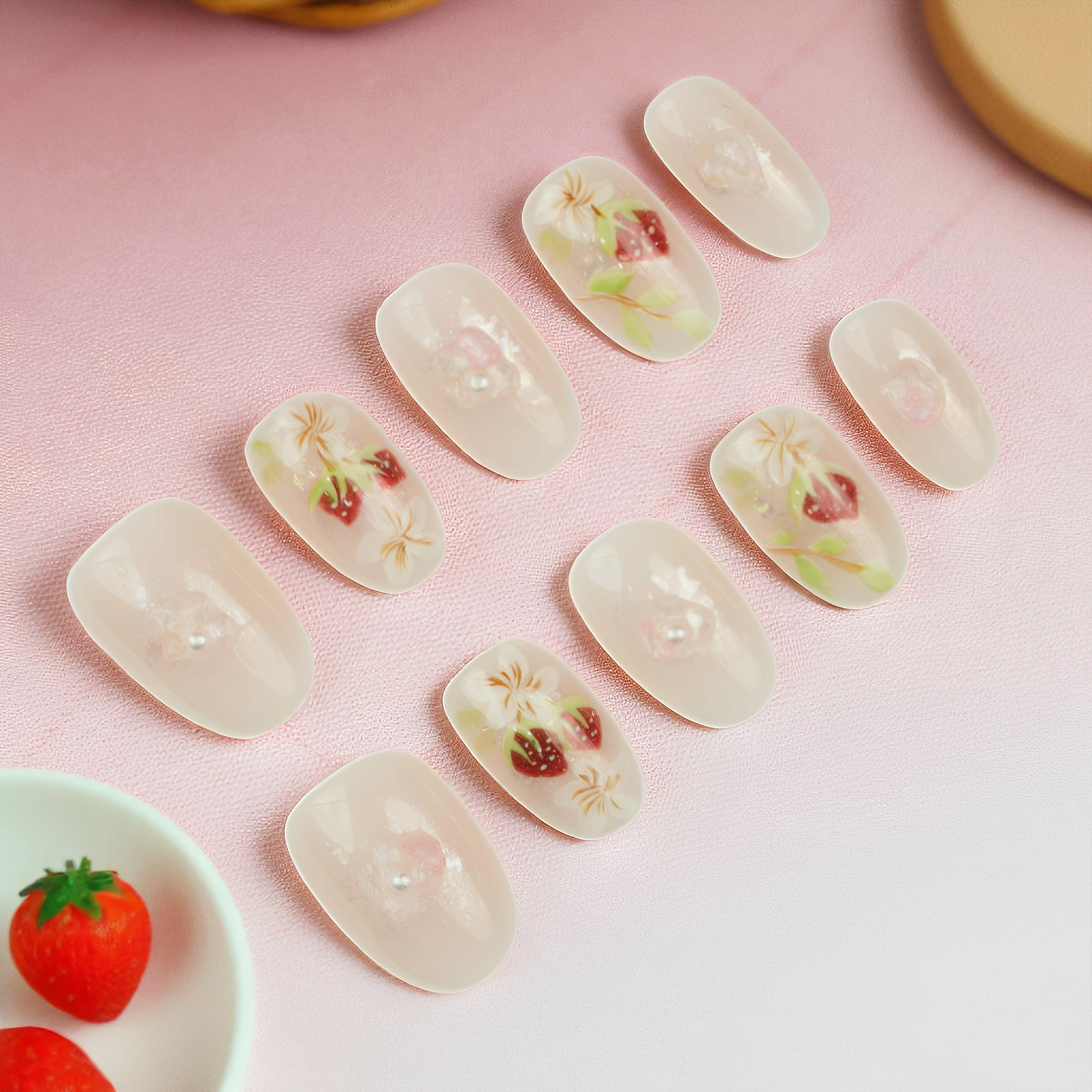 Nail art set with red strawberries, white flowers, pearl accents, and shimmer overlay