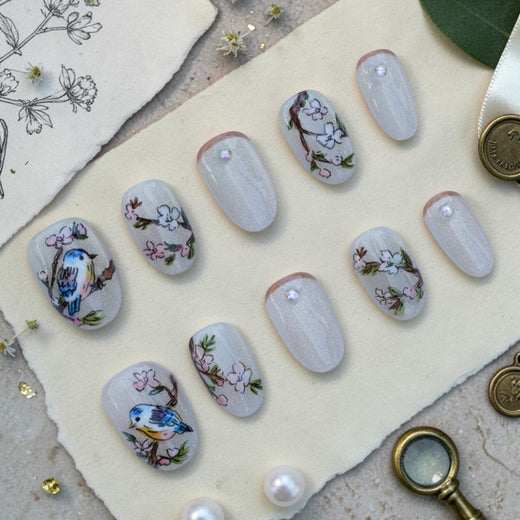 Handmade bird press on nails flat lay with hand painted songbirds and blossoms on a pearl cat eye base