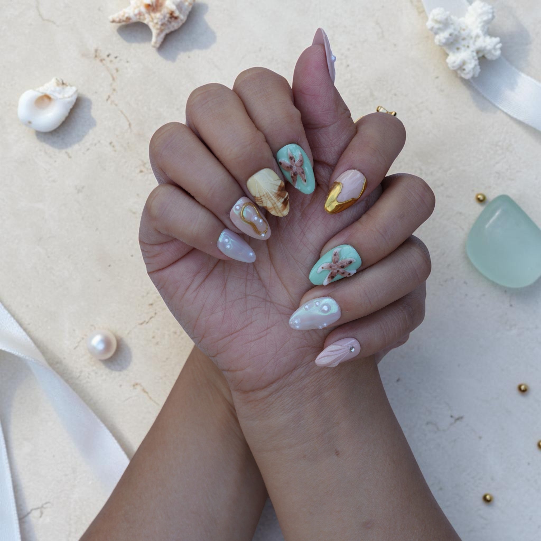 Tide Pool ocean press on nails shown on both hands with shells, starfish and gold