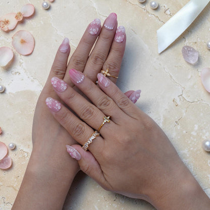 Pink cherry blossom press on nails worn on hand with pearl accents and gold rings