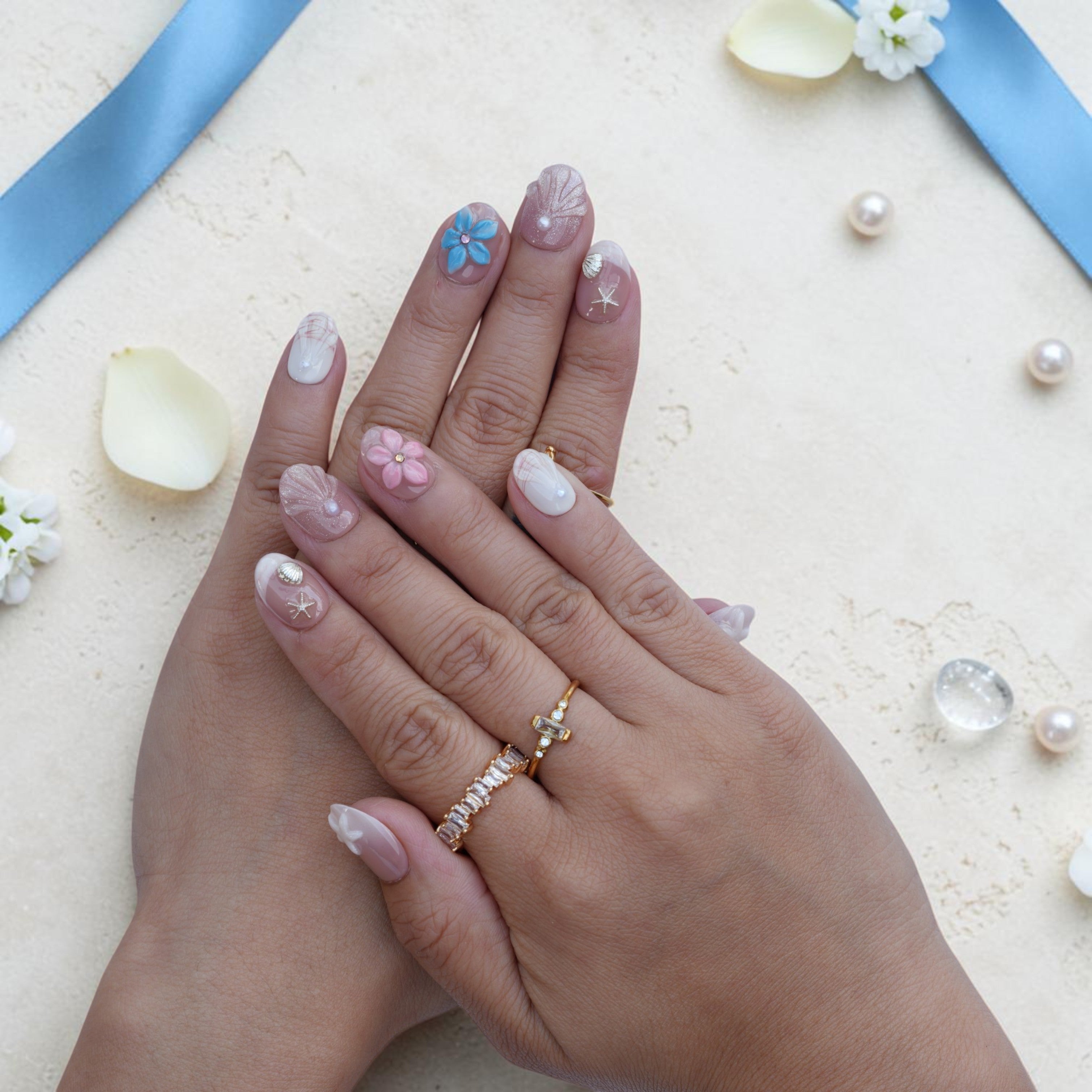 Pink and cream coastal press on nails worn on hand with 3D shells, pearls and a blue flower