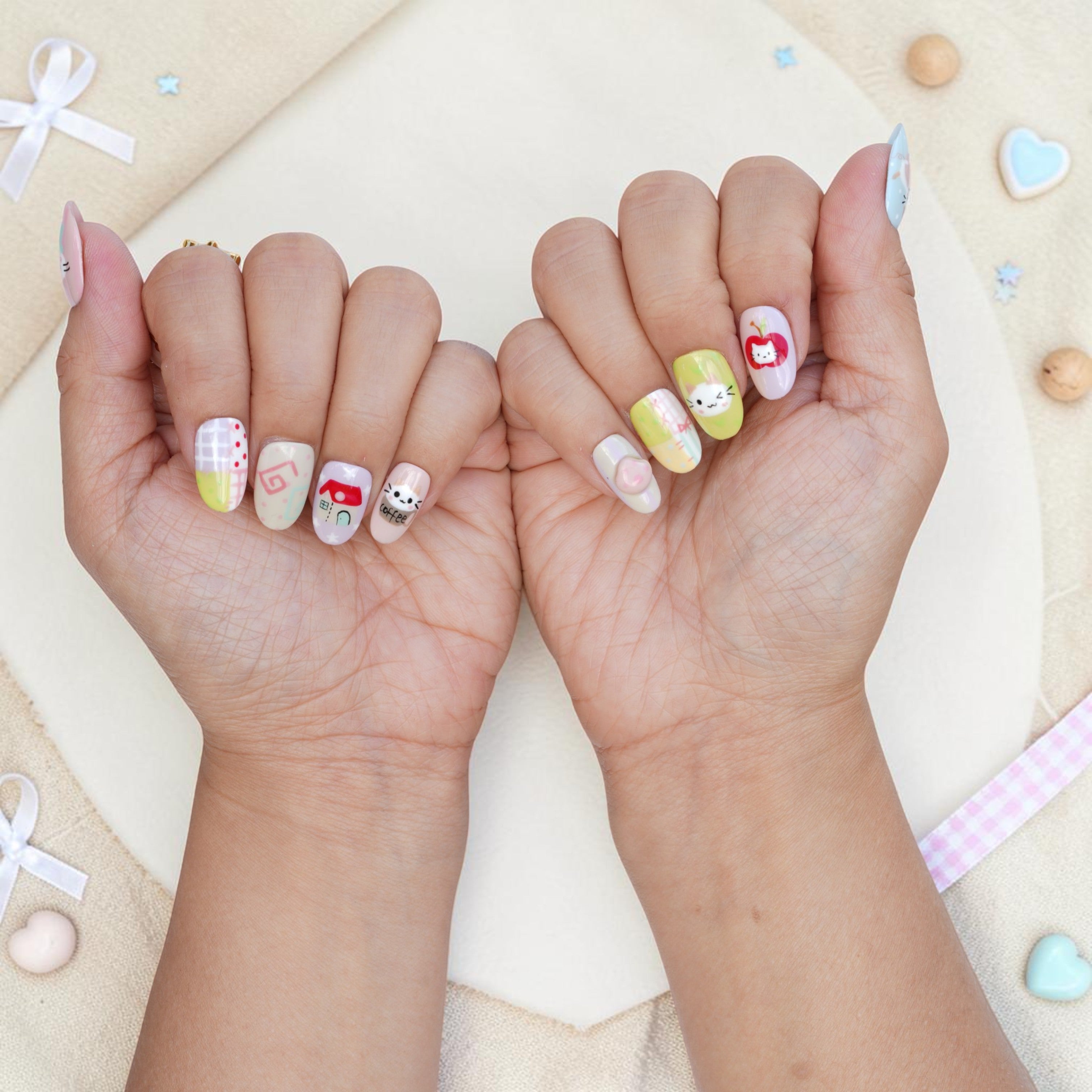 Both hands wearing kawaii cat press on nails in pastel pink, mint and yellow