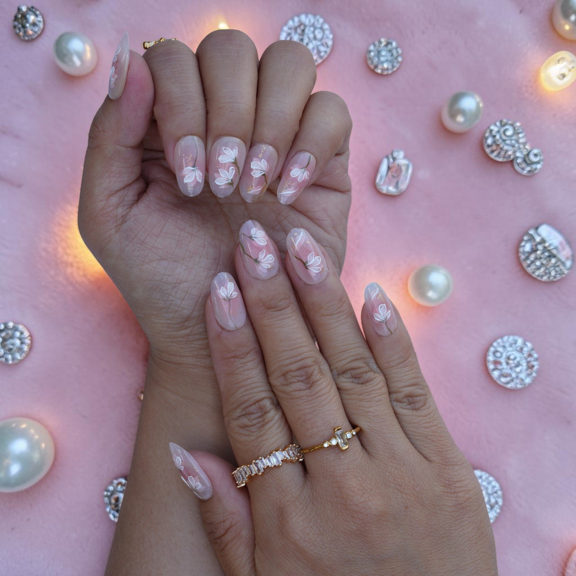Soft nude almond nails with white floral art and gold leaf on both hands