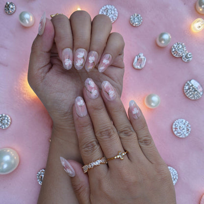 Soft nude almond nails with white floral art and gold leaf on both hands