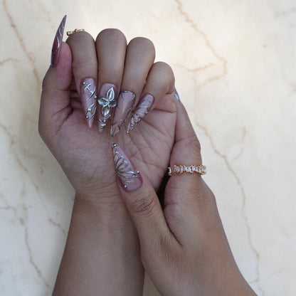 Hand wearing mauve stiletto nails with silver 3D flowers and heart line art