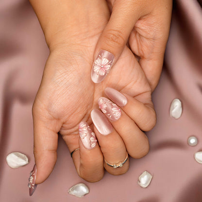Almond-shaped floral press on nails styled with rings and cherry blossom background.