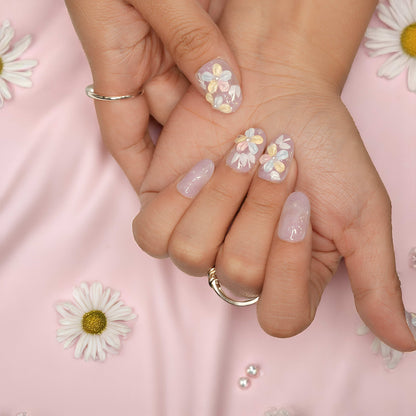 Close-up of fingers wearing handmade pastel flower press on nails, styled against lavender daisy-themed fabric.