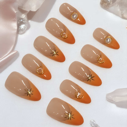 Sunset Nova press on nails laid out, featuring orange French tips with gold star, moon, and pearl embellishments