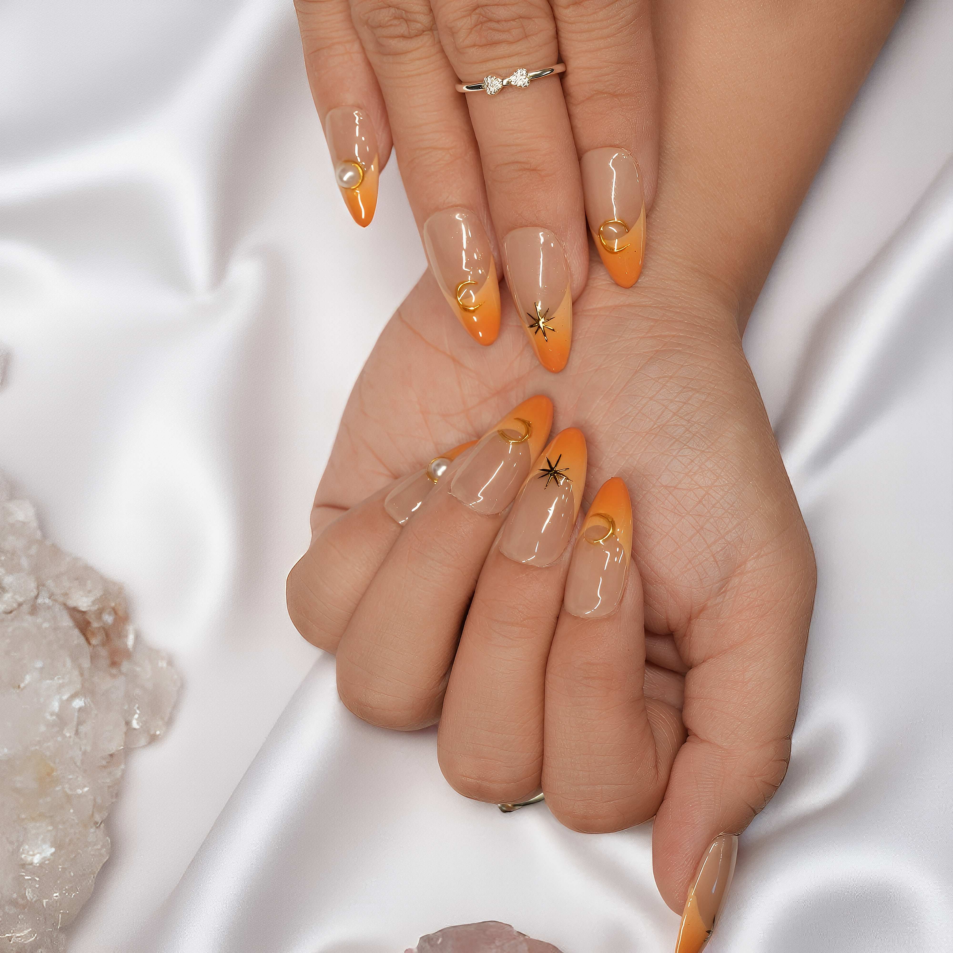 Front-facing view of Sunset Nova nails with orange French tips and soft celestial embellishments