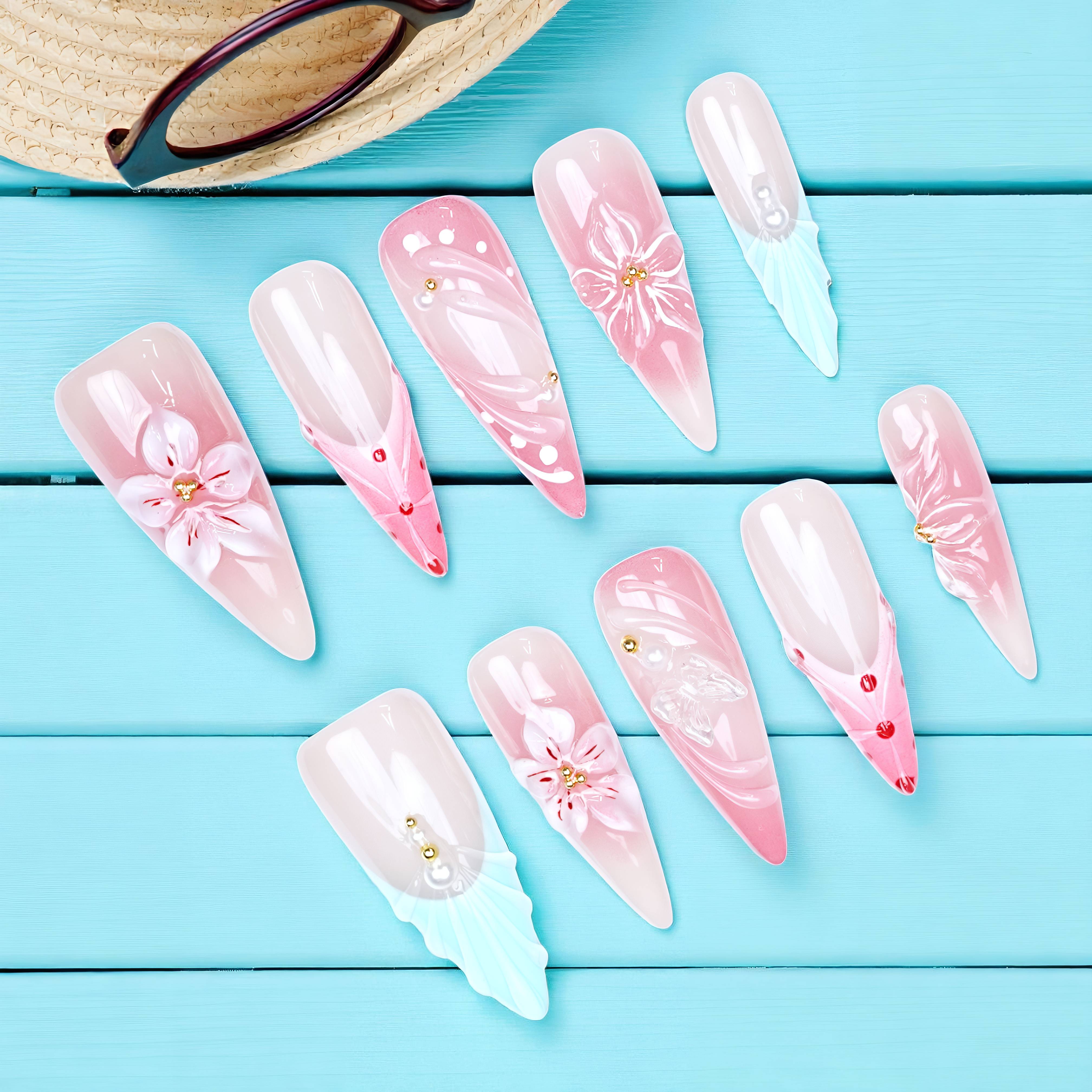 Flat lay of pink and aqua floral press on nails set with pearls, displayed on a blue wood surface