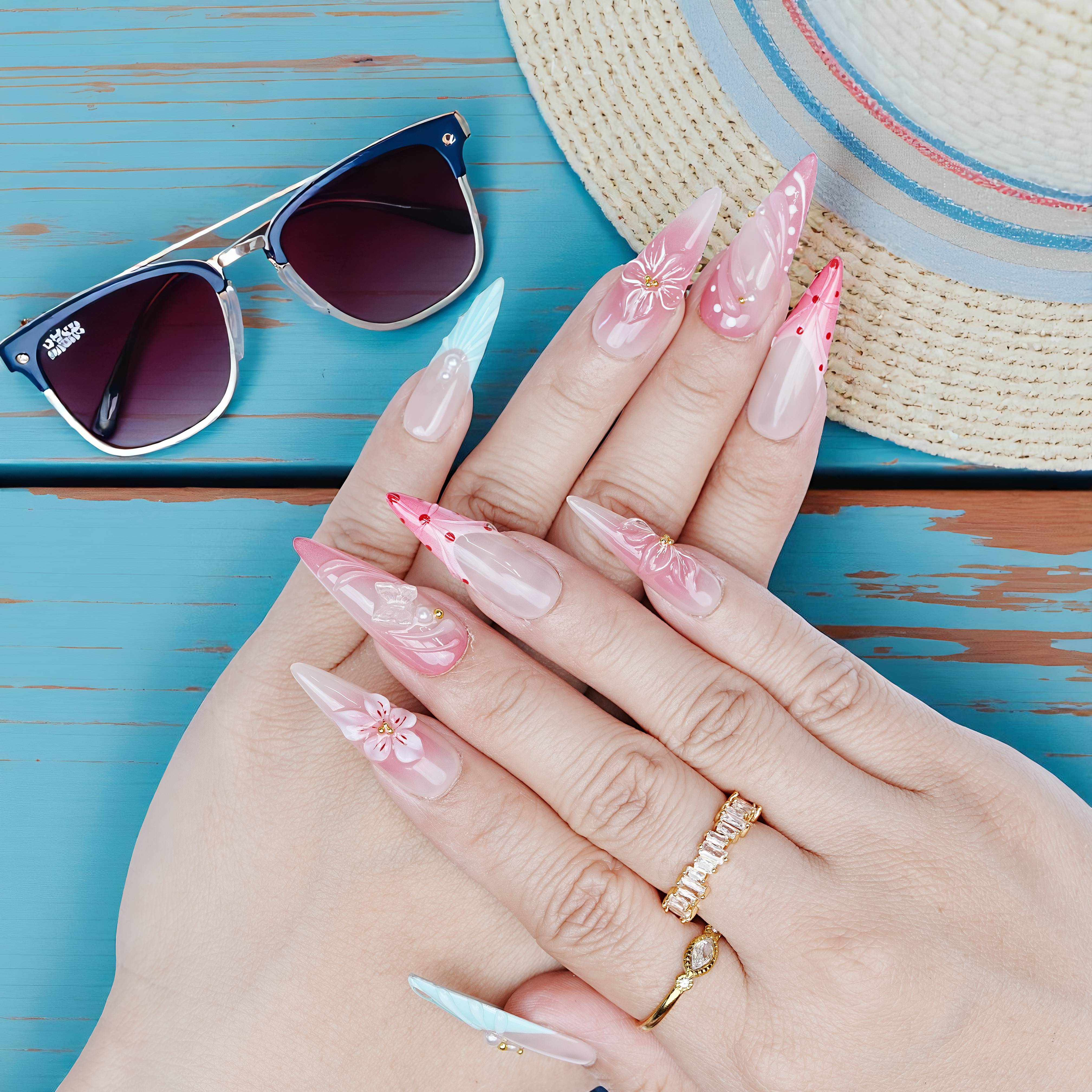 Hands wearing pink and aqua summer-themed press on nails with floral accents and shimmer under sunhat and sunglasses