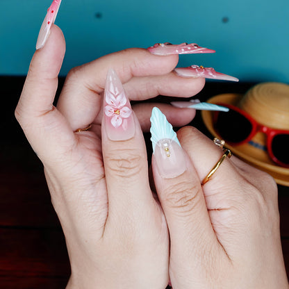 Hands displaying long stiletto press on nails with alternating aqua tips and pink floral patterns under moody lighting