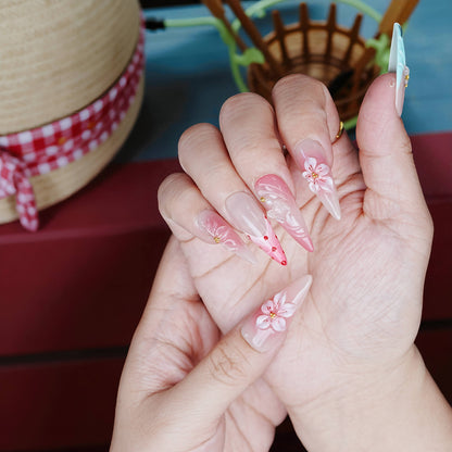 Natural light shot of floral press on nails set against a red deck and straw hat, showcasing vibrant coral tones