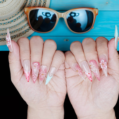 Symmetrical hand view of coral and aqua press on nails with hand-painted flower details and shimmer finishes, beach sunglasses background