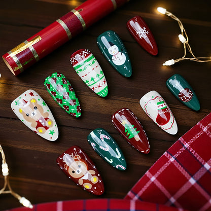 Flat lay of Christmas press on nails featuring Santa, snowflakes, candy canes, green knit patterns, and gingerbread men on dark wood background
