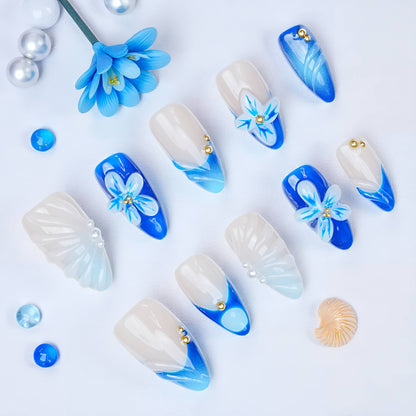 Top view of Blue Mirage press on nails on display. Features ocean blue tips, 3D sculpted white flowers, pearlescent shimmer, and almond shapes.