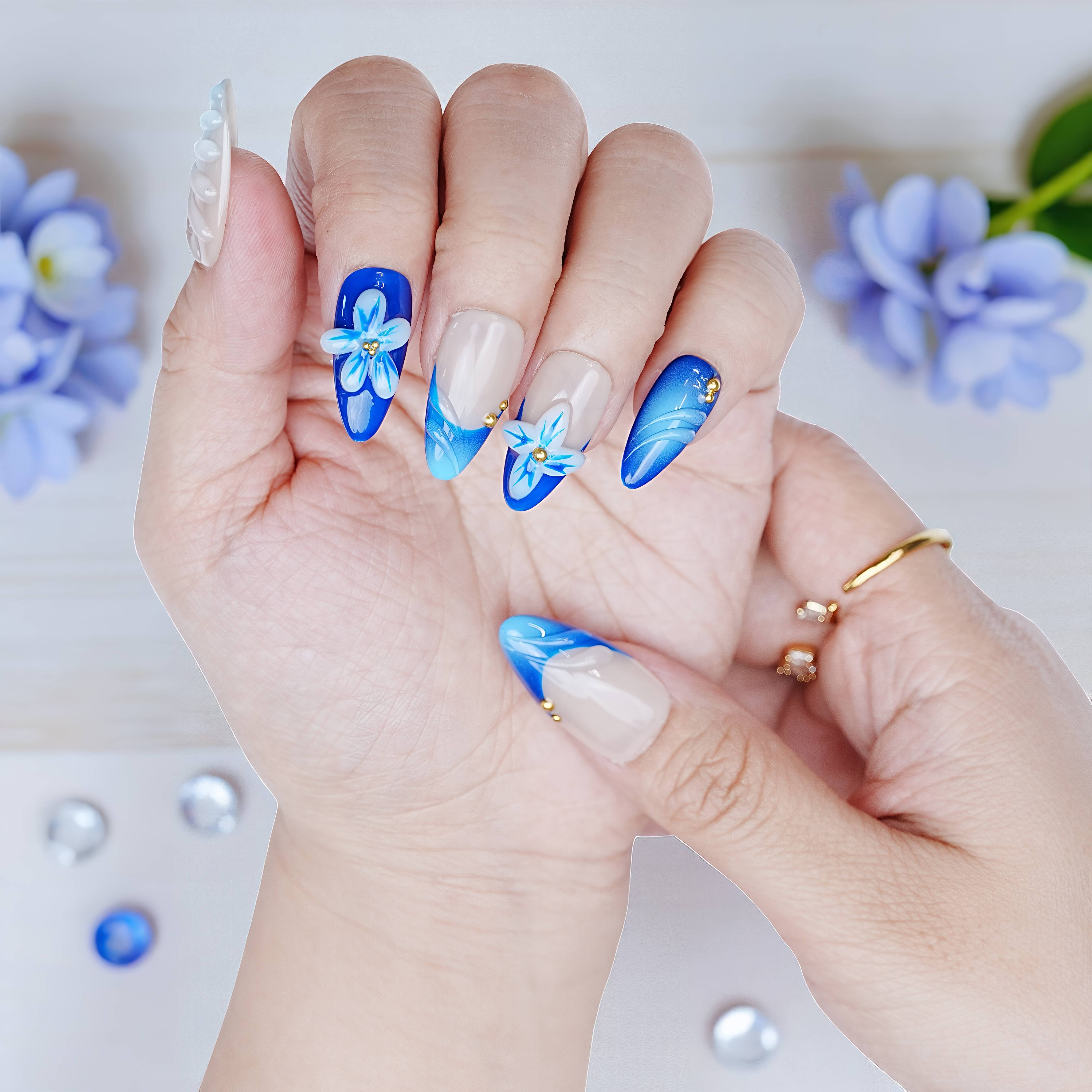 Both hands styled with ice blue press on nails featuring sculpted white flowers and ombré blue gloss.