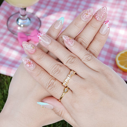 Hand pose showing Peachy Petal nails with floral and pink swirl details, styled with soft drinks and gold rings.