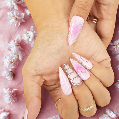 Flat lay of pink press on nails showcasing chrome designs, cosmic orbs with gemstones, sculpted heart, and celestial star details